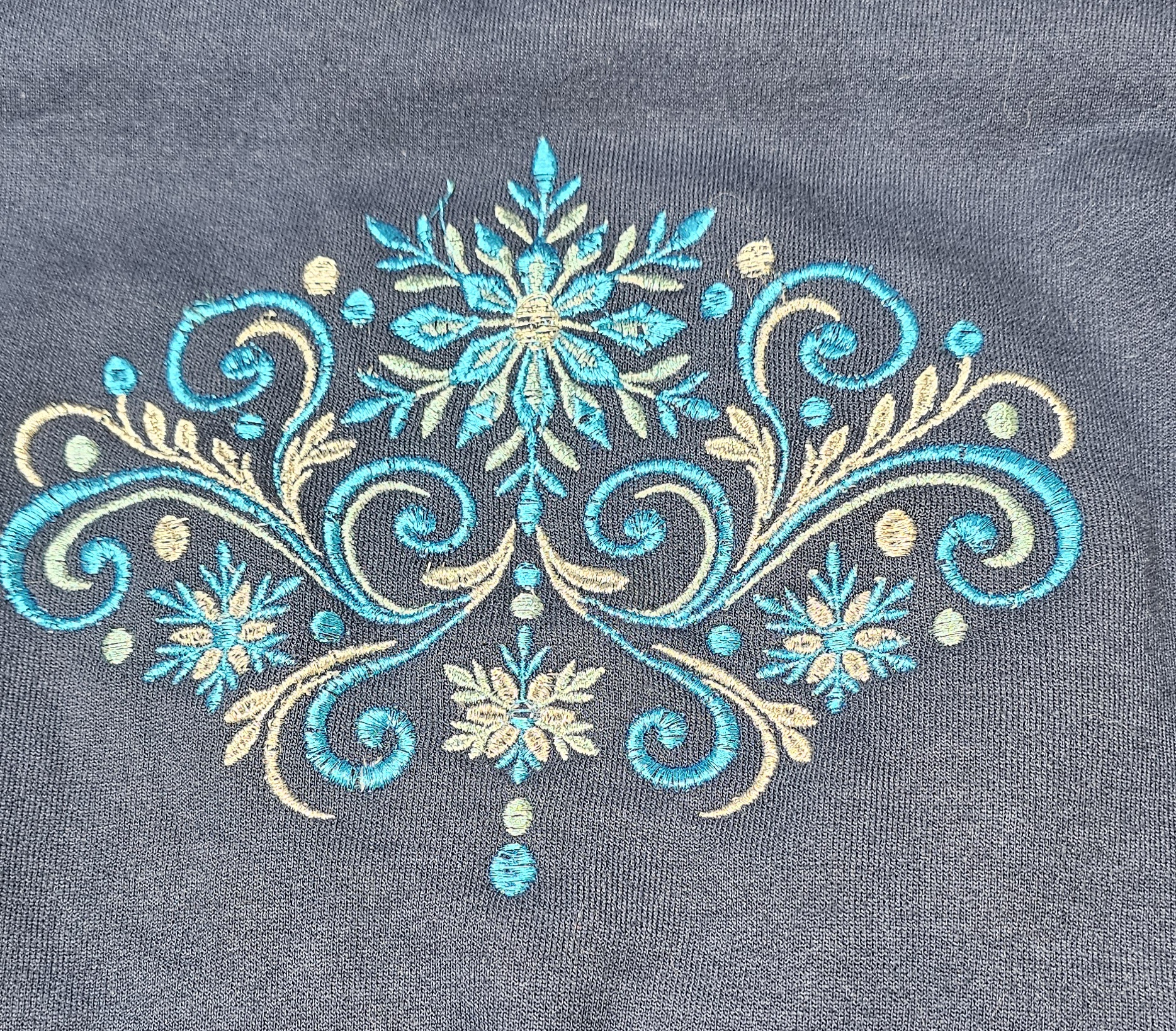 Teal and gold snowflake flourish embroidered on navy apparel