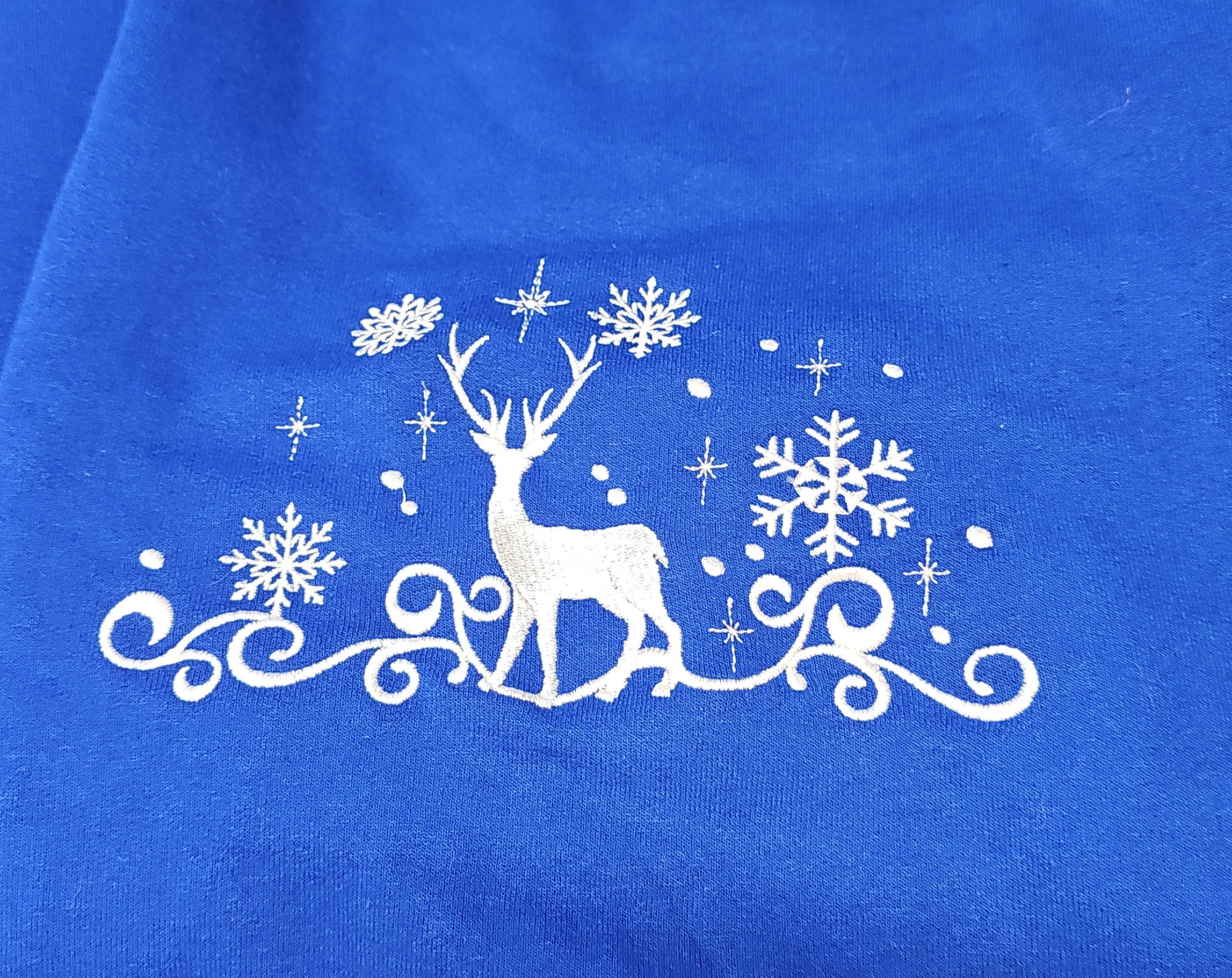 White winter deer and snowflakes embroidered on royal blue apparel