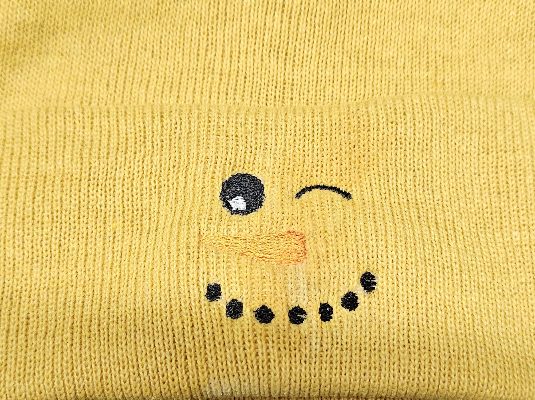 Winking snowman face embroidered on a mustard yellow beanie