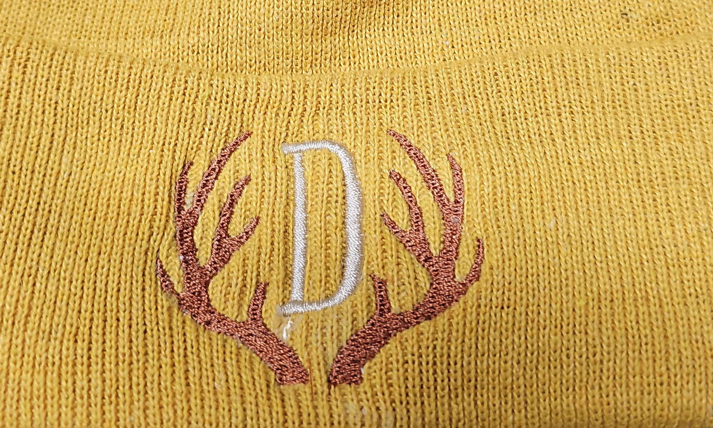 Monogram letter D framed by antlers embroidered on a mustard beanie