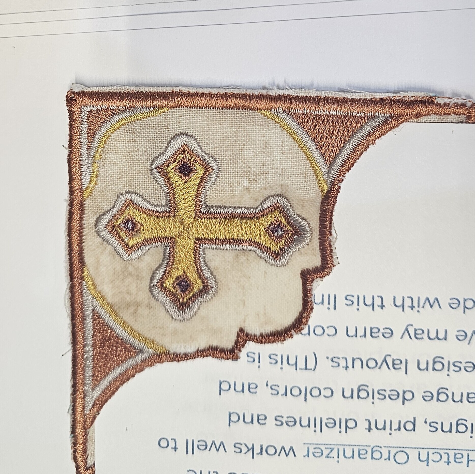 Embroidered corner bookmark with a gold cross and bronze trim