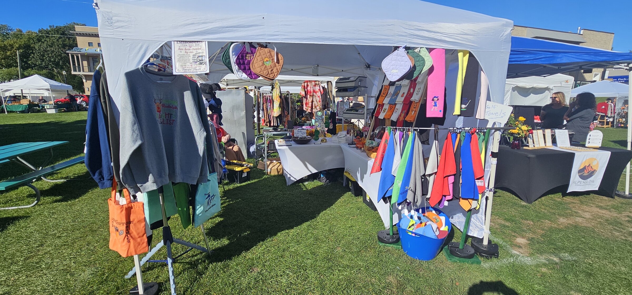 Outdoor Fanciful Threads craft fair tent with embroidered sweatshirts, bags, and colorful towels
