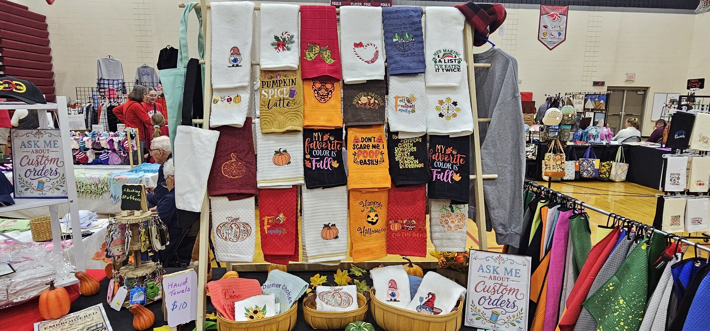 Fanciful Threads craft fair booth with embroidered towels, bags, and custom orders signs