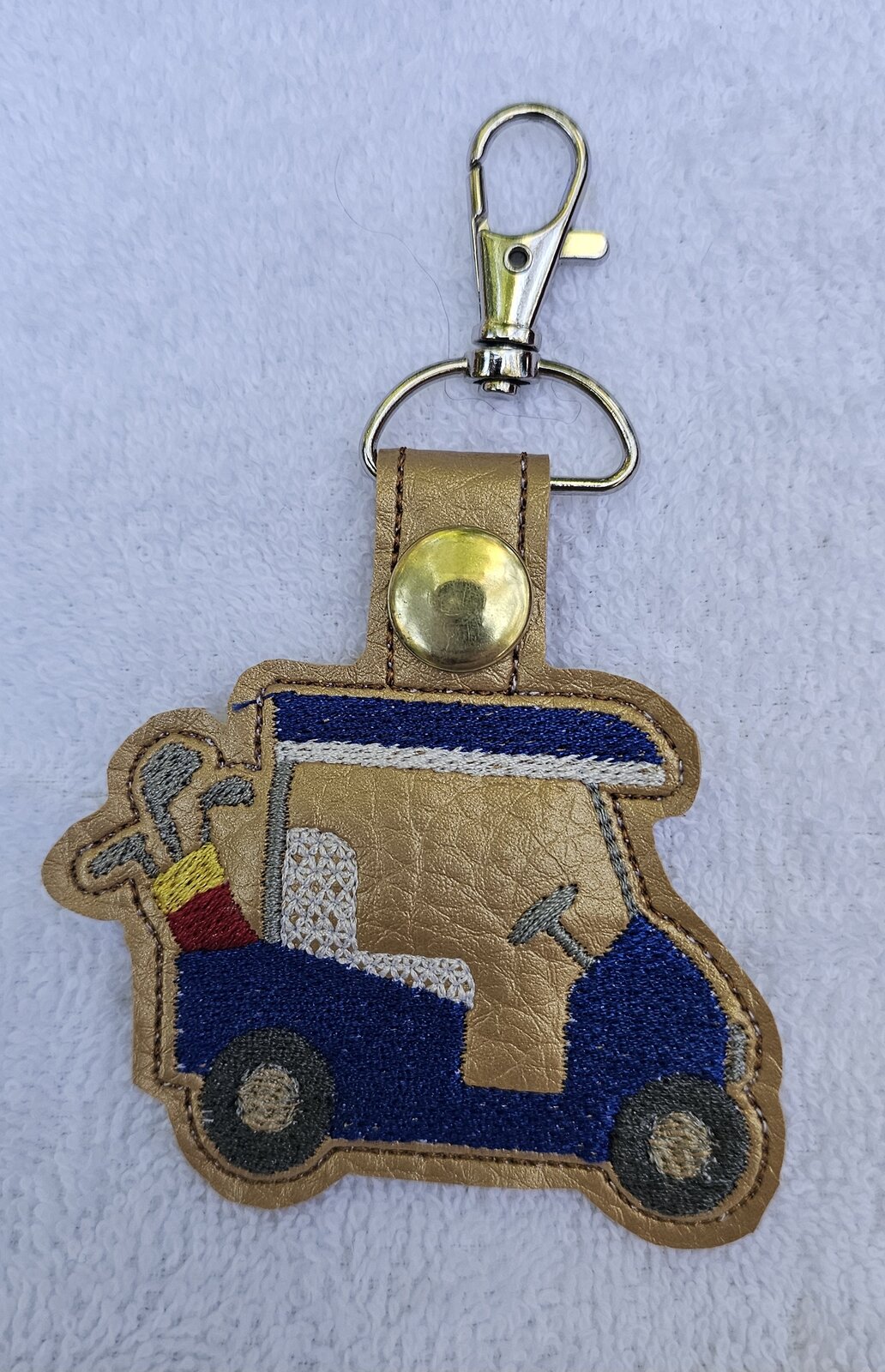 Gold key fob embroidered with a blue golf cart carrying clubs