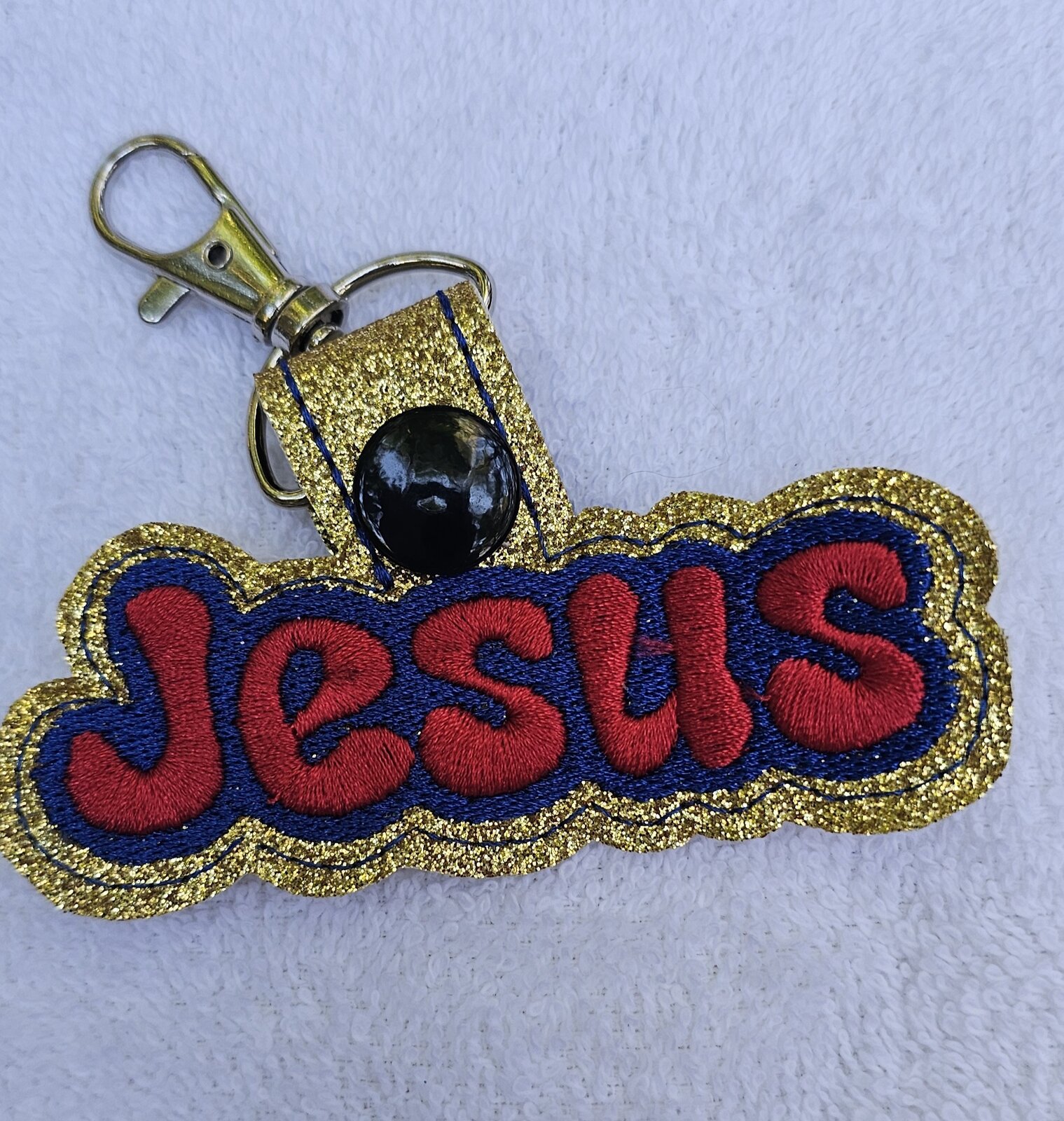 Gold glitter key fob embroidered with the word Jesus in red and navy