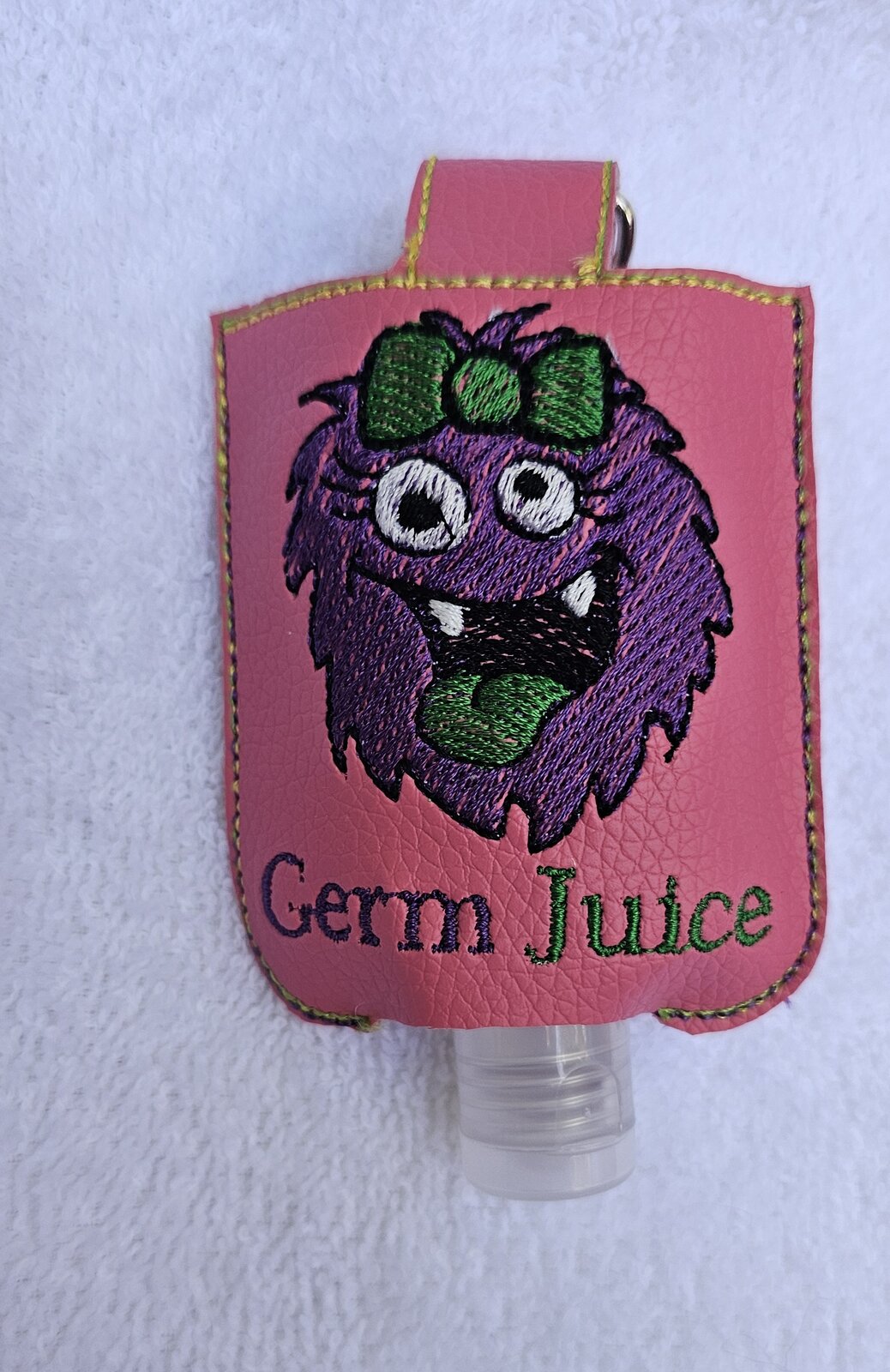 Pink embroidered hand sanitizer holder with a purple monster and the words Germ Juice