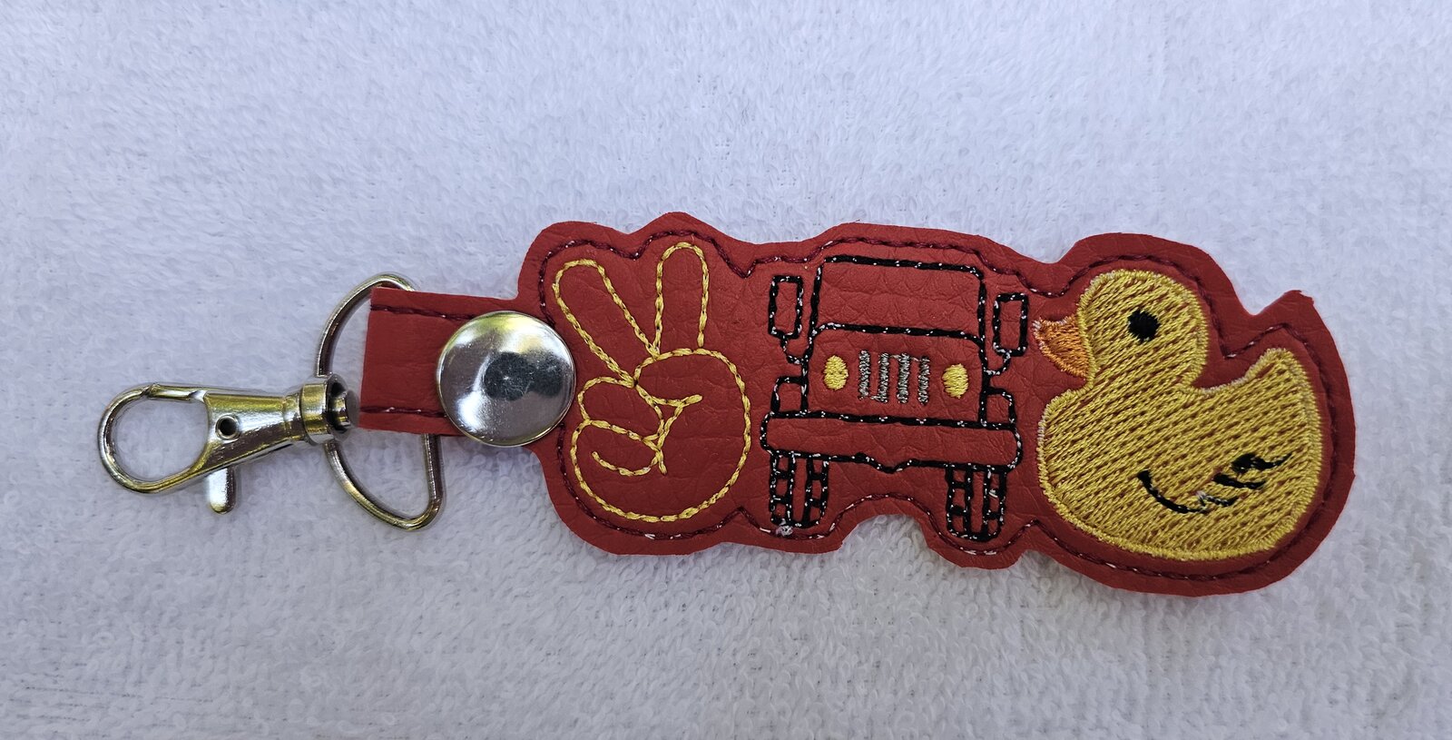 Red key fob embroidered with a peace sign hand, a Jeep, and a rubber duck