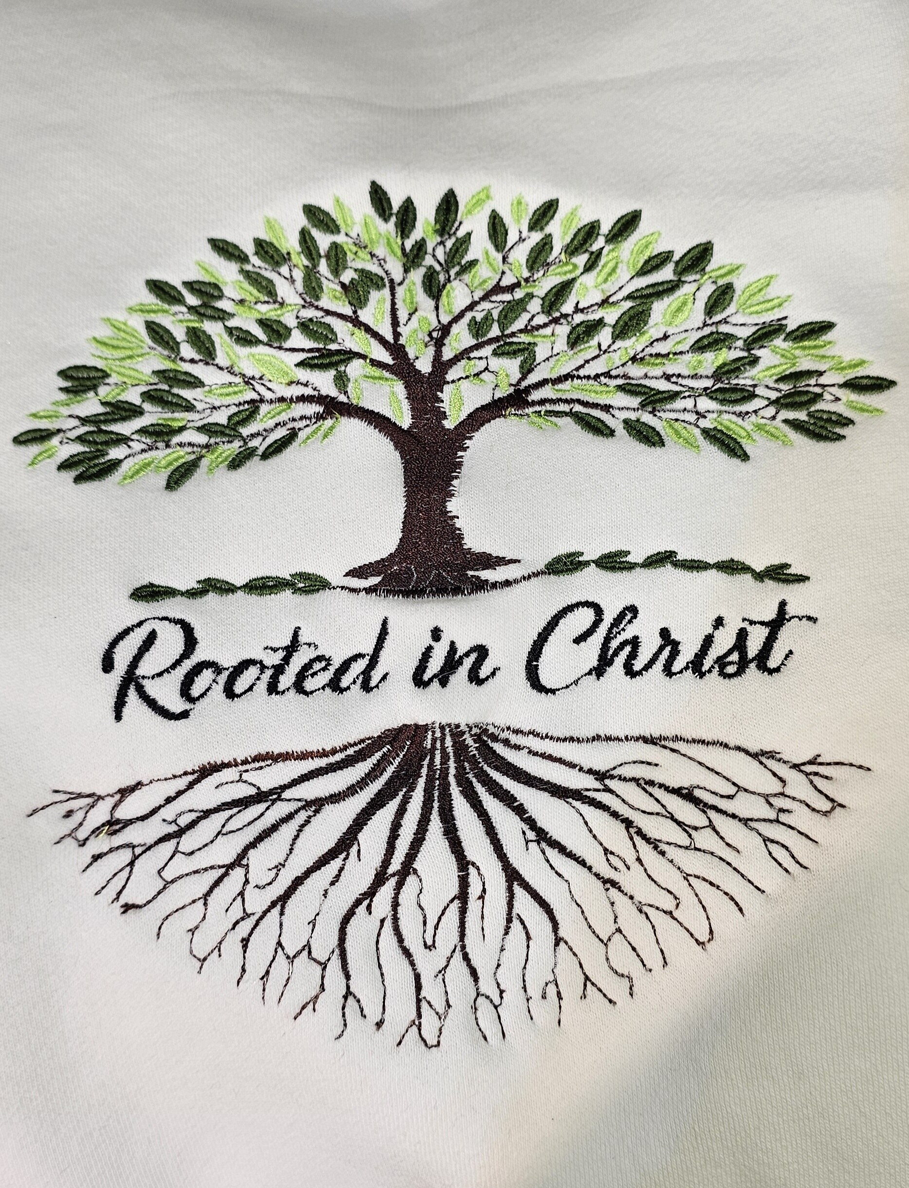 Tree and roots embroidered on white apparel with the phrase Rooted in Christ