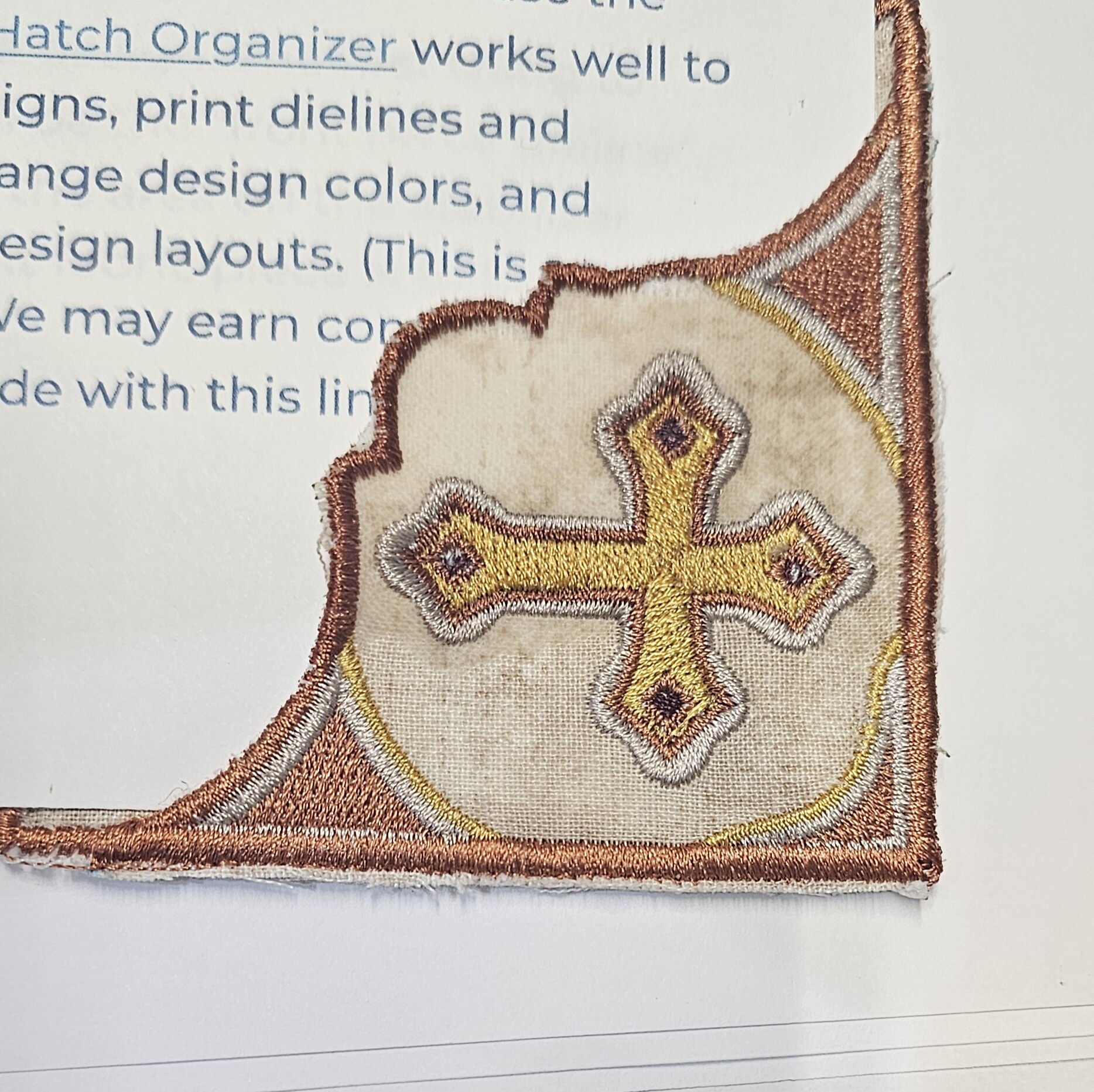 Embroidered religious corner book marker with a gold cross and bronze trim